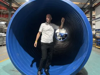 Person standing inside a large-diameter blue HDPE structured-wall pipe